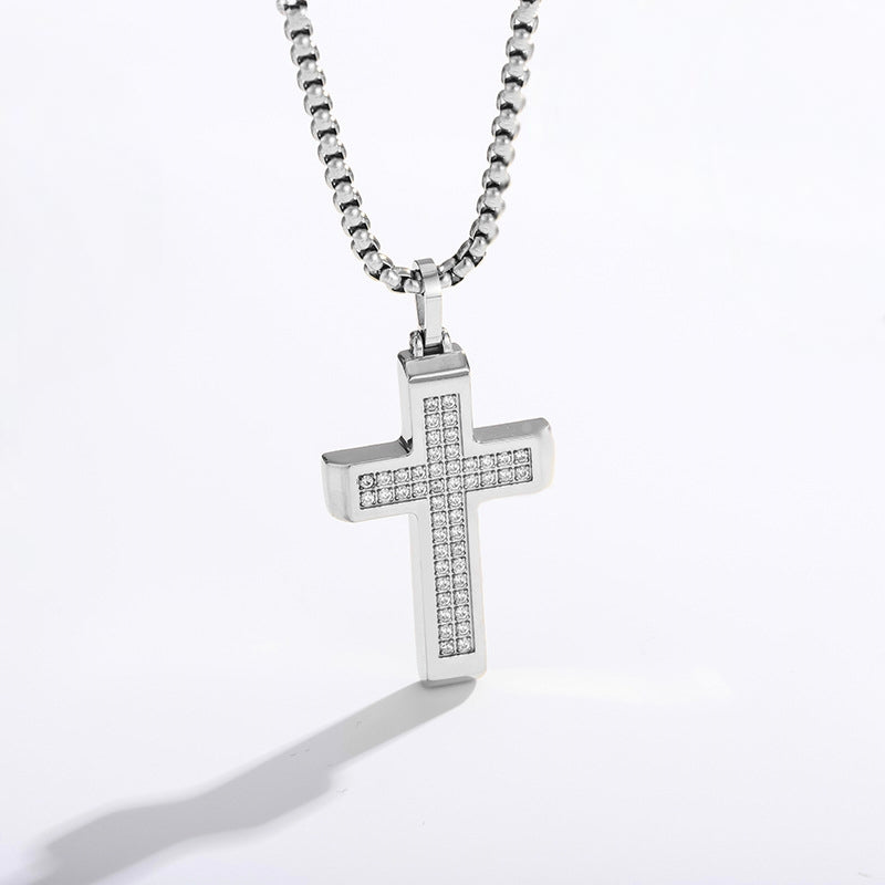 A silver cross pendant necklace paved with small clear stones, hanging from a silver box chain against a white background.