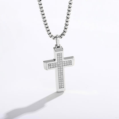 A silver cross pendant necklace paved with small clear stones, hanging from a silver box chain against a white background.