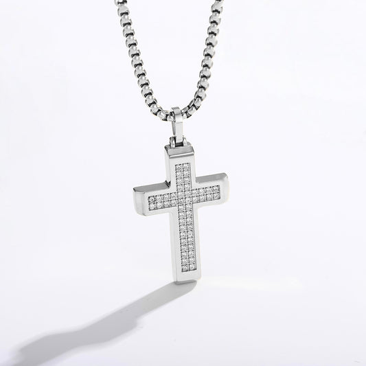 A silver cross pendant necklace paved with small clear stones, hanging from a silver box chain against a white background.
