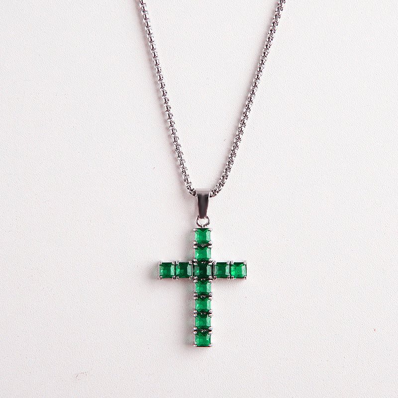 A silver cross pendant necklace adorned with multiple rectangular green gemstones, suspended from a silver ball chain against a plain white background.