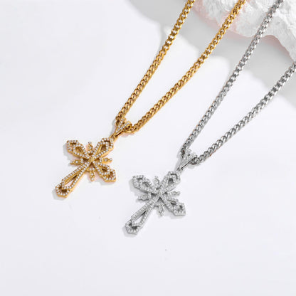 Two cross-shaped pendant necklaces with pavé-set stones, one in yellow gold and one in silver, displayed on a clean white background with a small piece of white shell prop.