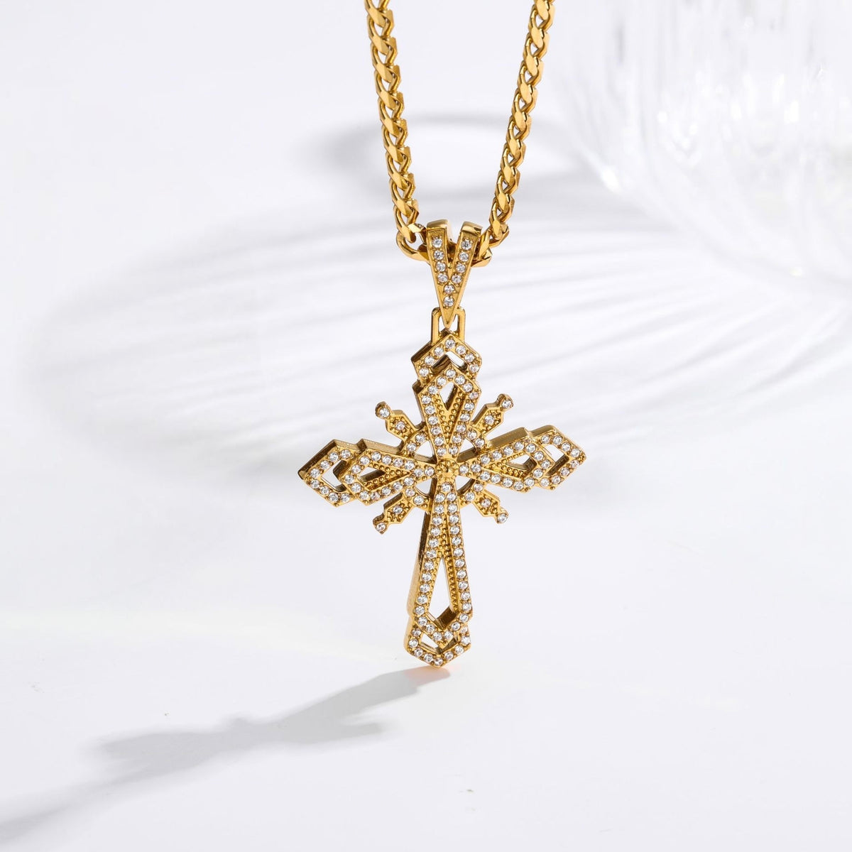 A gold cross pendant necklace encrusted with small clear stones, hanging from a gold chain on a white background.