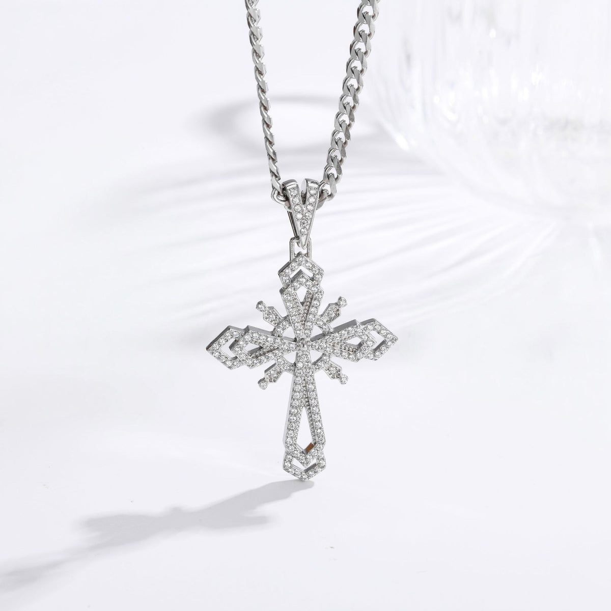 A silver-toned cross pendant necklace paved with small clear stones, hanging from a matching chain on a clean white background.