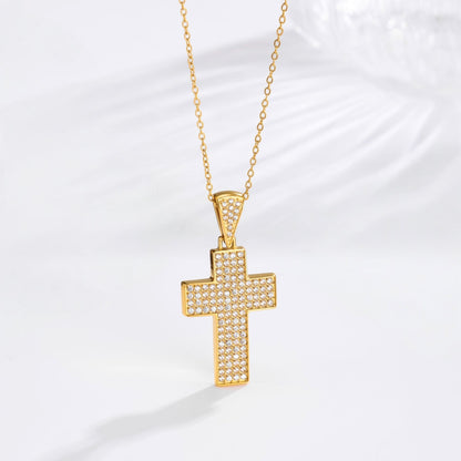 A gold cross pendant necklace paved with small clear stones, hanging from a delicate gold chain against a white background with a soft shadow.