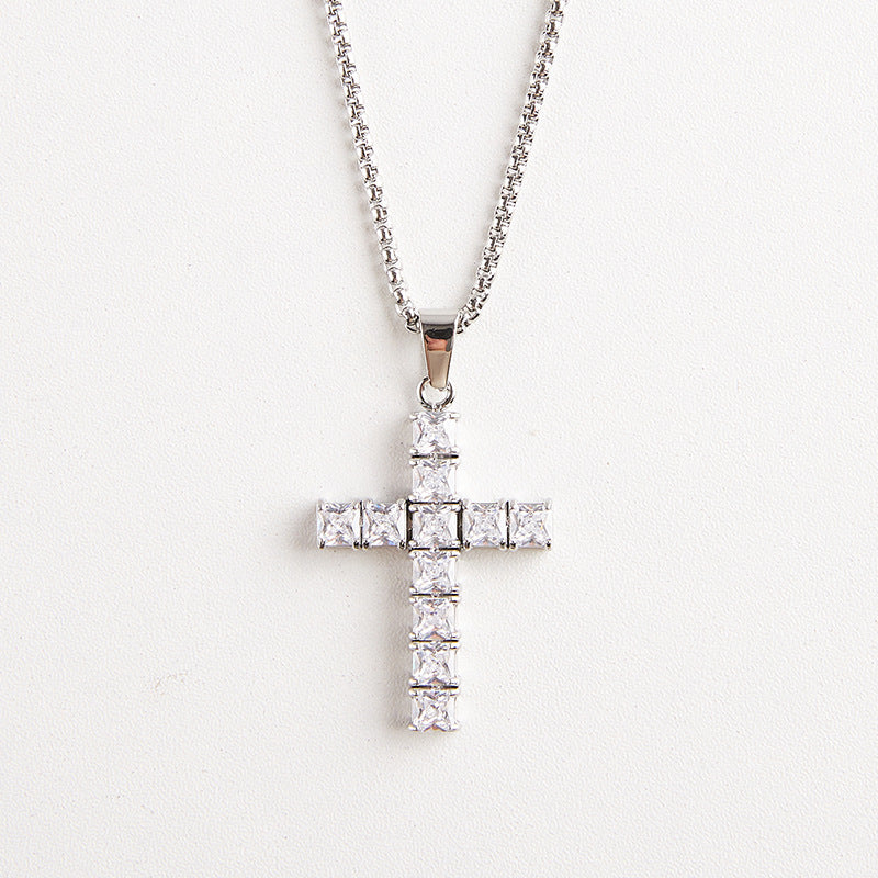 A silver cross pendant necklace adorned with clear square-cut stones, hanging from a silver chain against a plain white background.