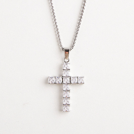 A silver cross pendant necklace adorned with clear square-cut stones, hanging from a silver chain against a plain white background.