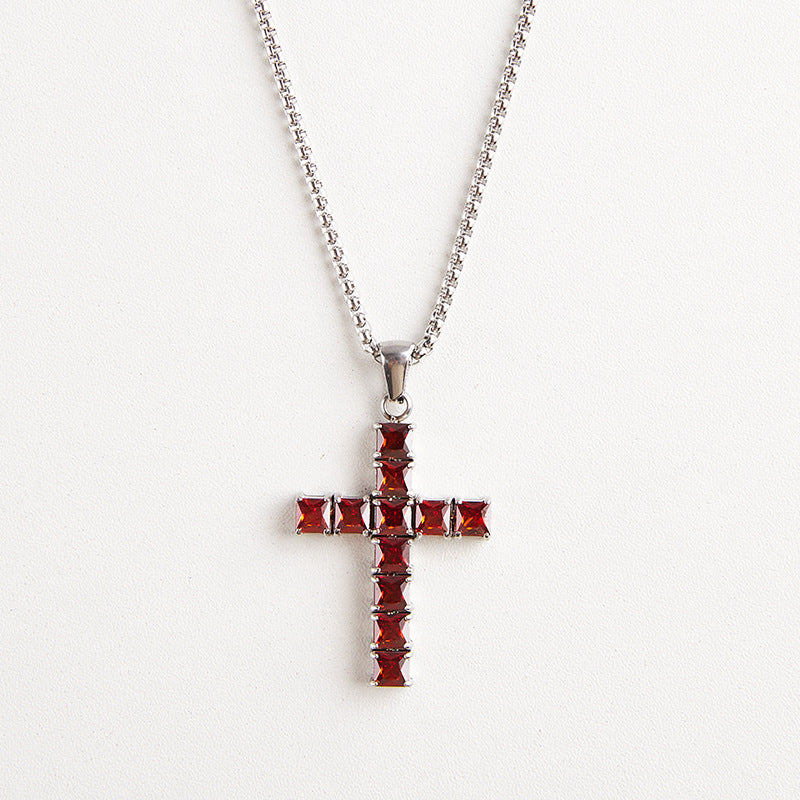A silver cross pendant necklace adorned with faceted red gemstones, suspended from a silver ball chain against a plain white background.