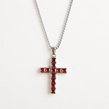 A silver cross pendant necklace adorned with faceted red gemstones, suspended from a silver ball chain against a plain white background.