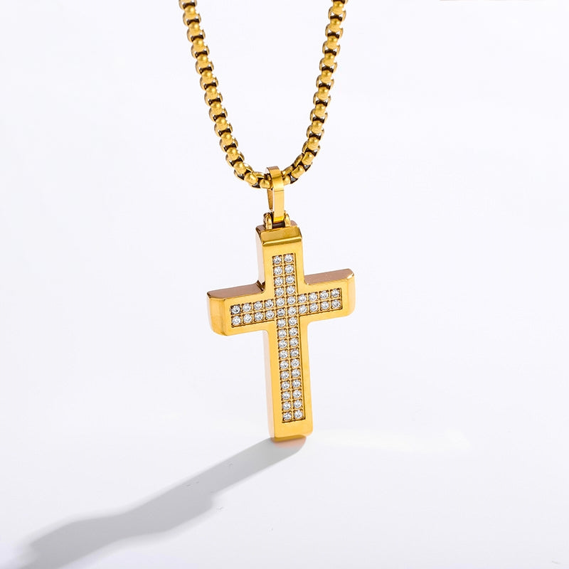 A gold cross pendant necklace with a channel-set row of clear cubic zirconia stones on the front, suspended from a gold box chain against a white background.