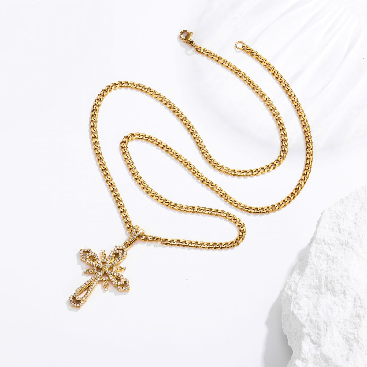 A gold-toned chain necklace with a decorative cross pendant, styled on a white textured surface.